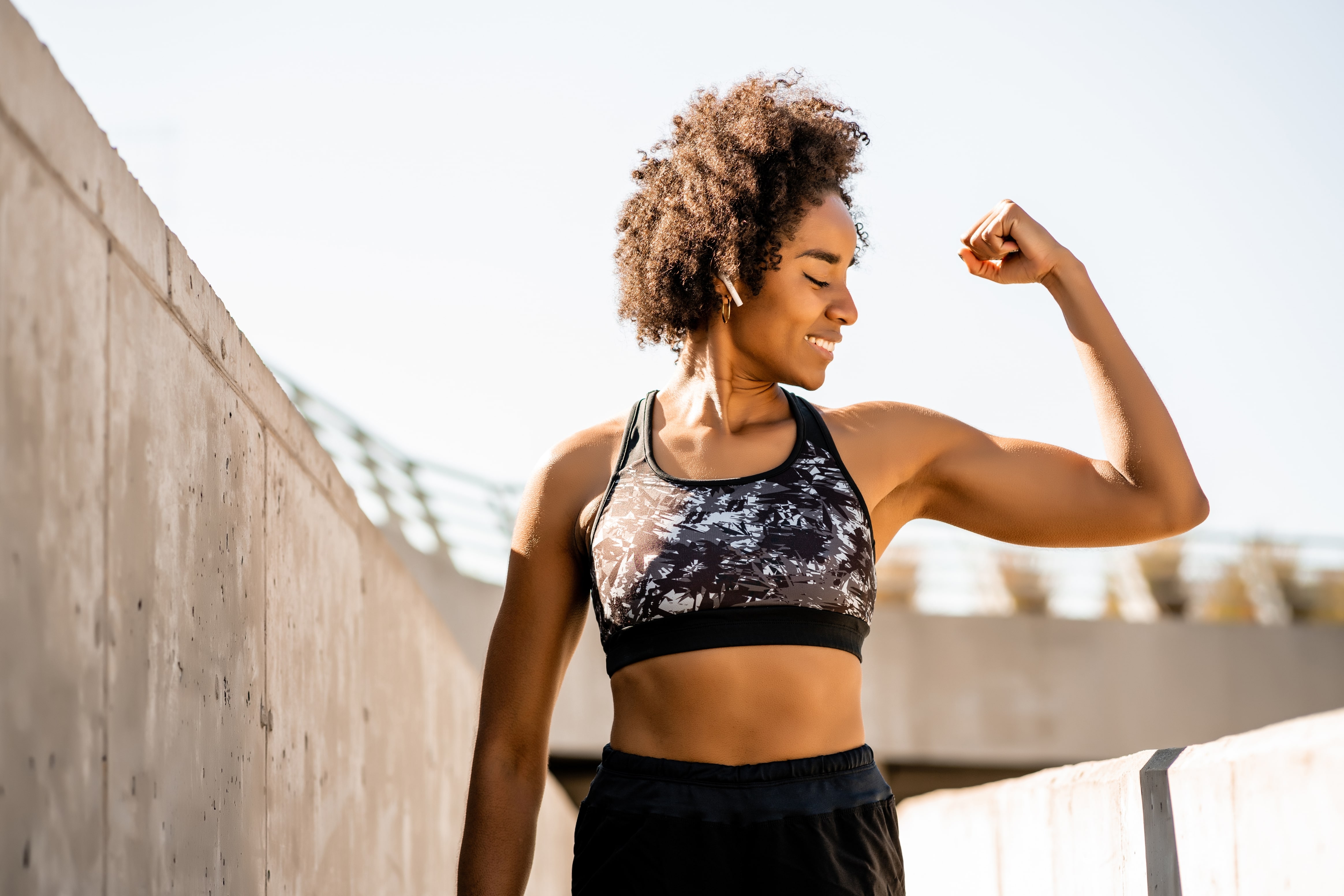 Afro female athlete flexing her muscles outdoors